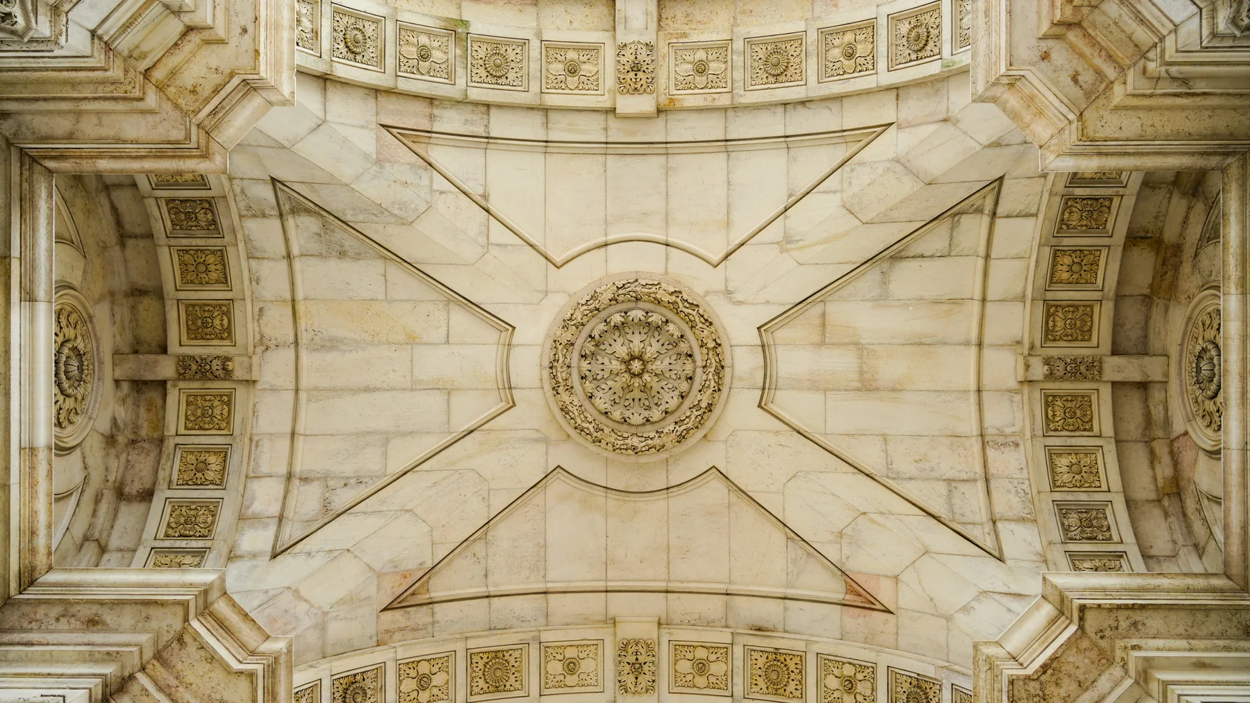 Symmetrical classical stone ceiling with detailed carvings and a central medallion.