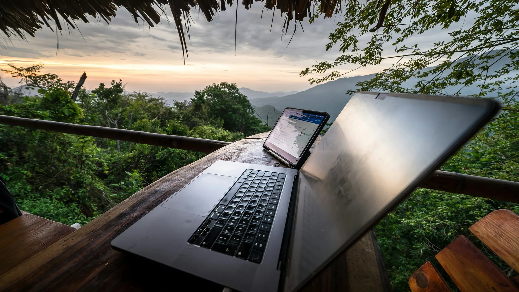 Laptop and smartphone on a wooden terrace overlooking a mountain landscape.