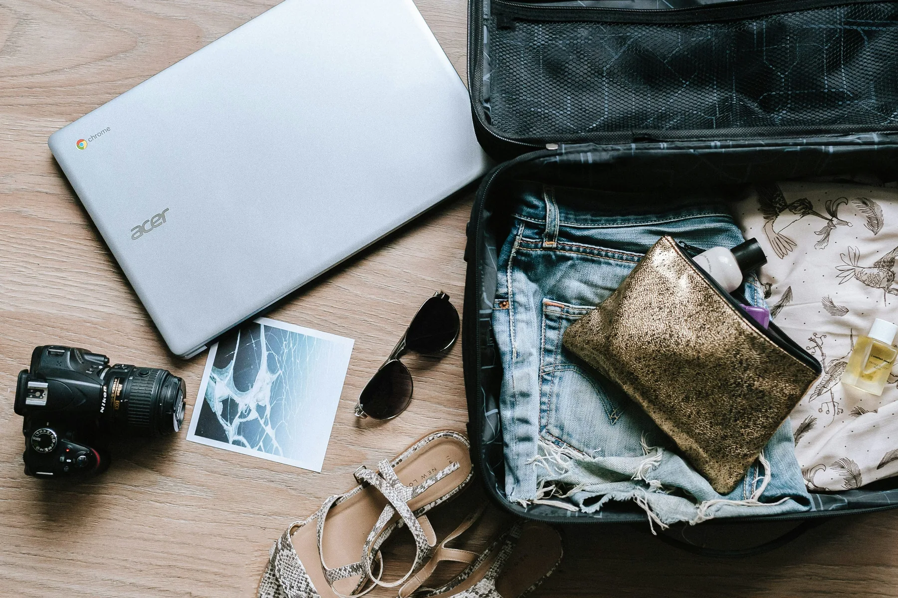 Open suitcase with travel equipment, camera and laptop prepared for a trip.