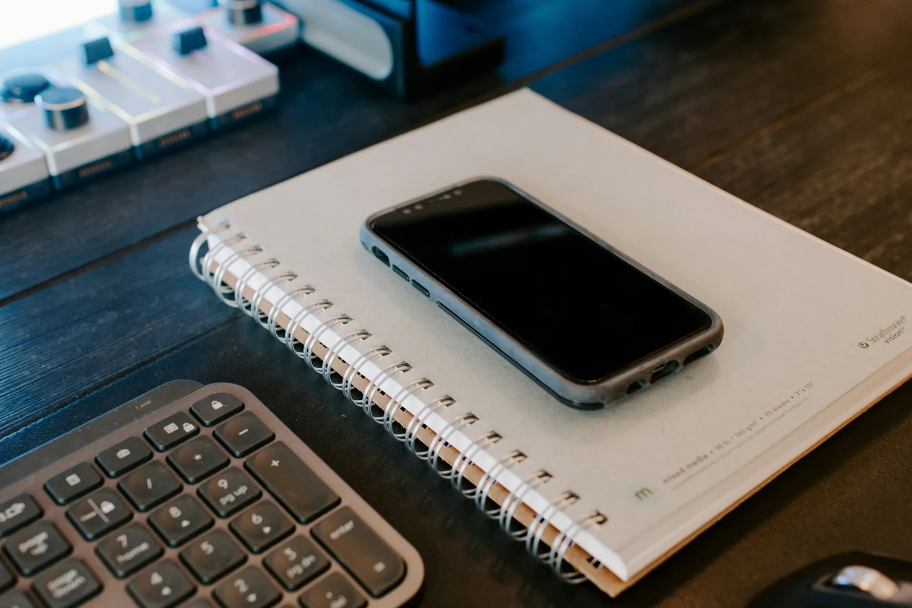 Smartphone resting on a notebook beside a keyboard in a calm workspace.