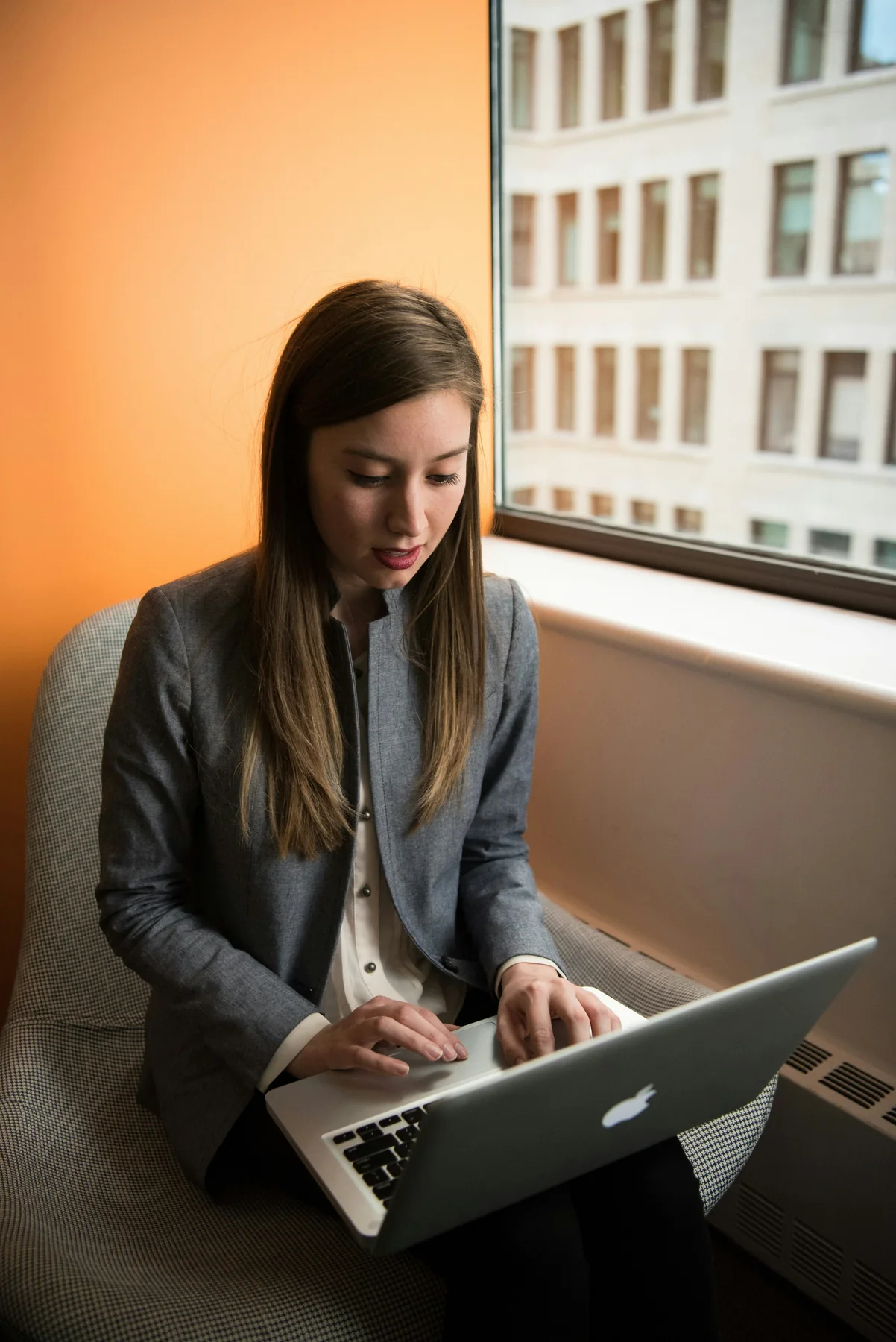 Woman working on a laptop beside a large window.