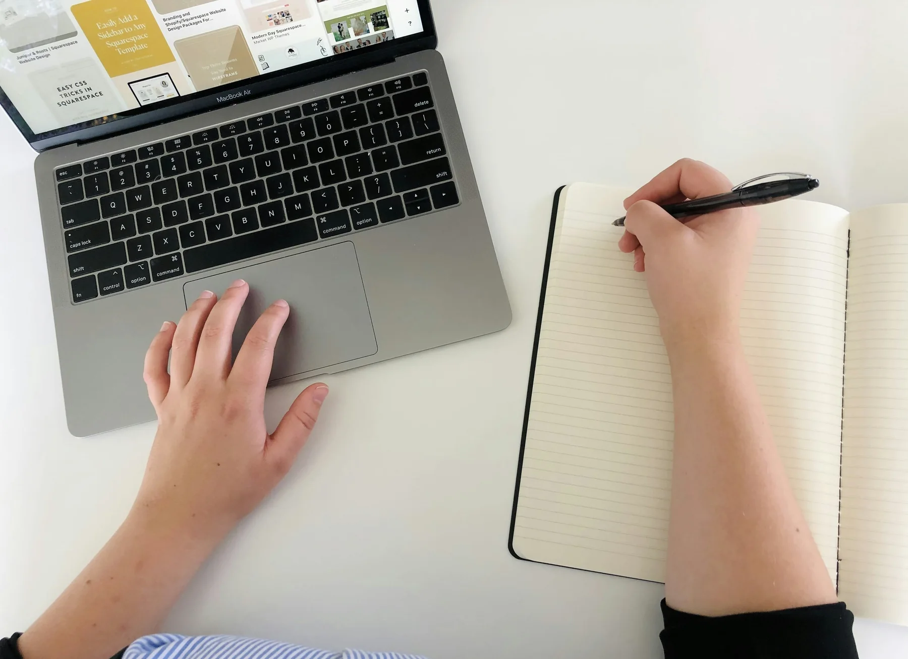Hands working between a laptop and an open notebook.