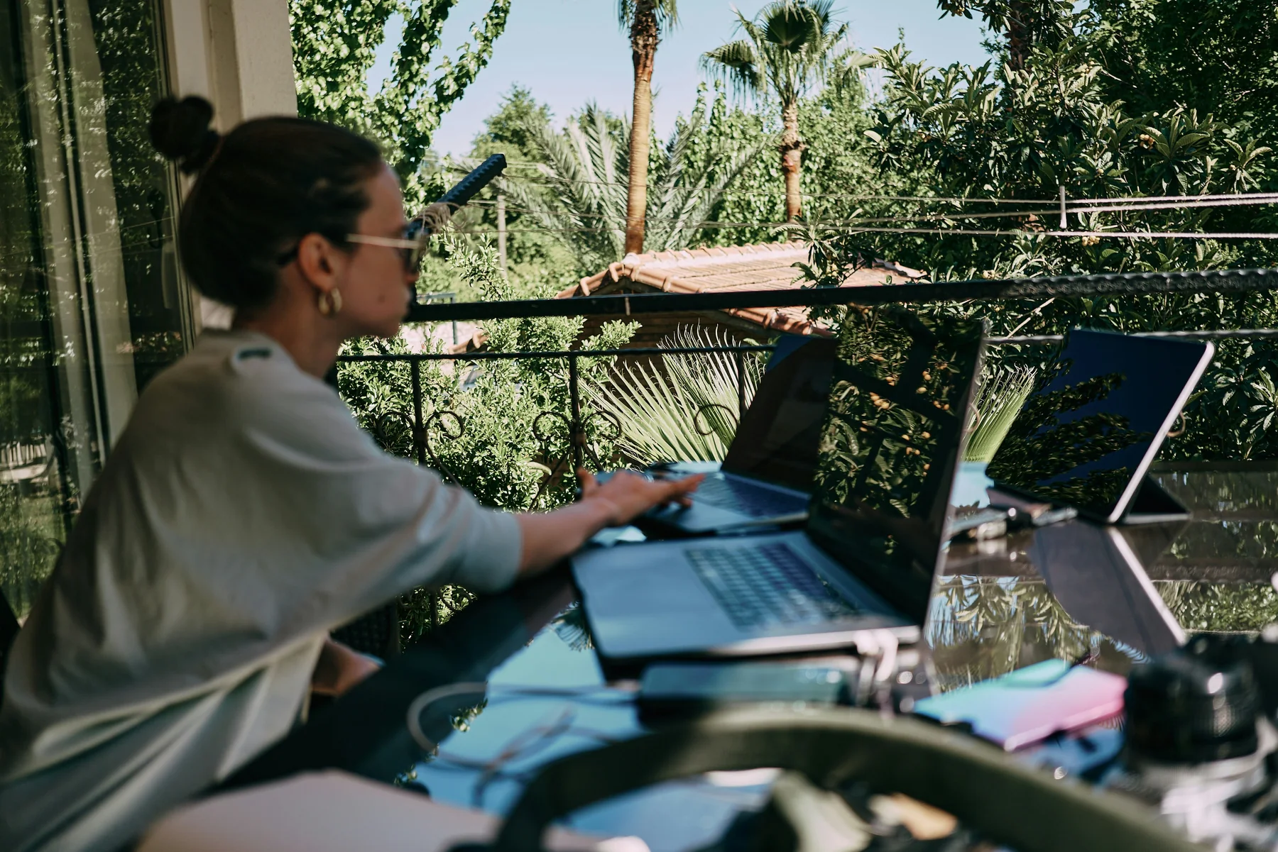A softly out-of-focus person working on a laptop at a leafy outdoor table.
