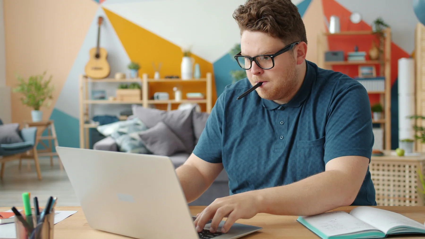 Man concentrating while working on a laptop in a colourful home workspace.