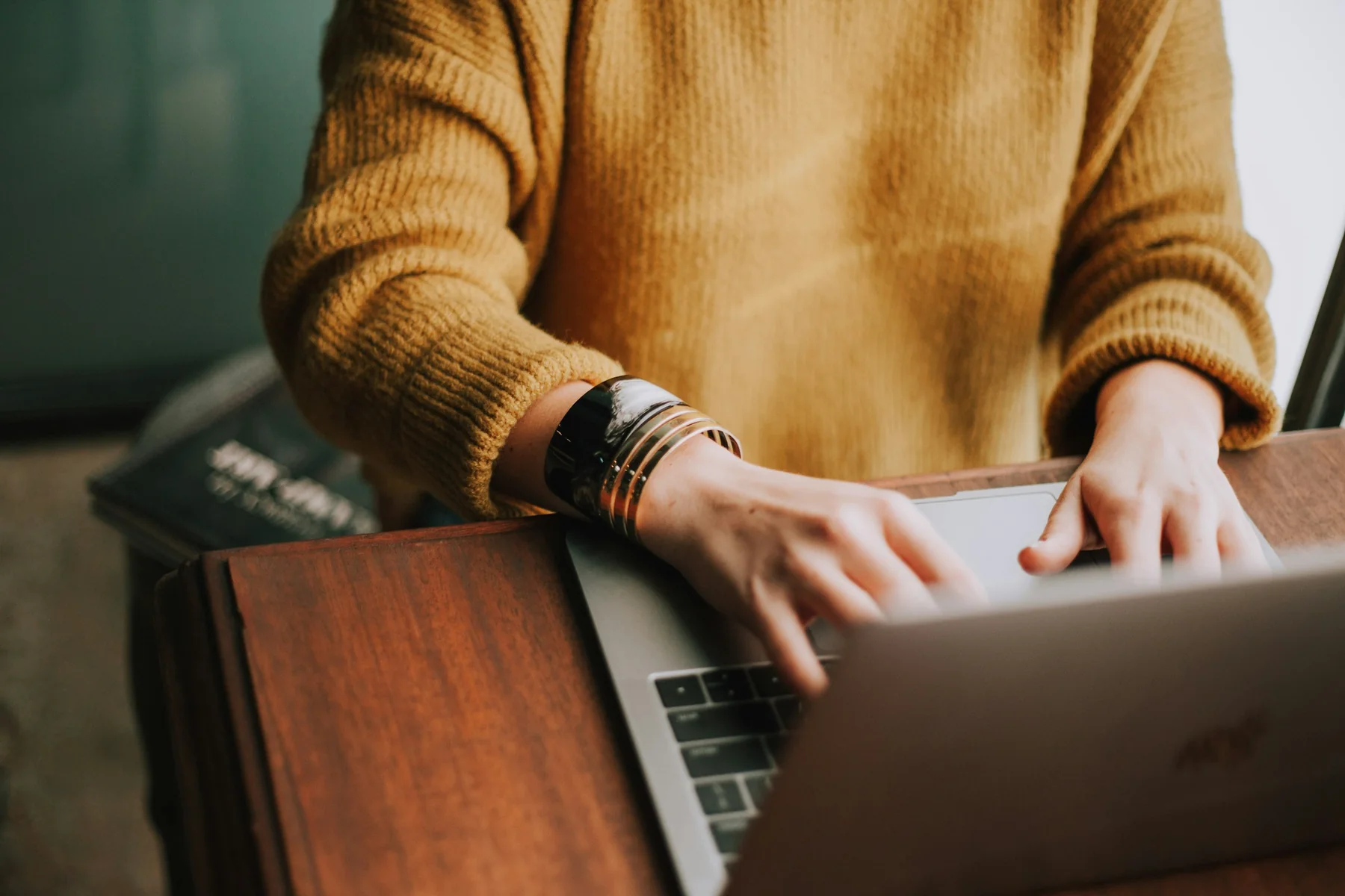 Close view of a person working on a laptop at a wooden table.