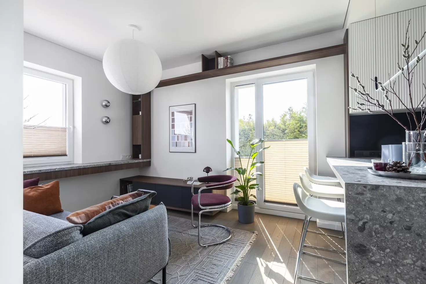 Sunlit modern apartment living room with balcony and kitchen beyond.